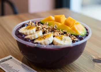 Bol de acaí comercial con granola, plátano, mango y miel junto a una etiqueta nutricional sobre mesa de madera