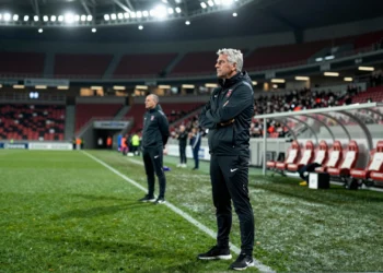 Entrenador de fútbol observa el campo con los brazos cruzados en la banda de un estadio internacional iluminado de noche