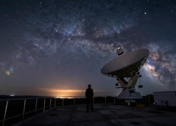 Más allá del arcoíris: el universo emite luz que nuestros ojos nunca podrán ver, y los astrónomos llevan décadas aprovechándola 2 Astrónomo silueteado junto a un radiotelescopio bajo un cielo nocturno con bandas de luz infrarroja y ondas de radio