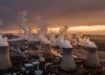 De fenómeno natural a emergencia planetaria: la larga historia del efecto invernadero que cambió el clima de la Tierra 6 Planta de carbón con columnas de humo frente a glaciares en retroceso bajo un cielo ámbar, símbolo del cambio climático