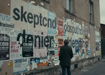 Del negacionismo a la obstrucción: cómo ha cambiado el lenguaje que describe a quienes bloquean la acción climática 6 Figura solitaria frente a un muro urbano con capas de carteles y palabras como "negacionista" y "obstruccionista"