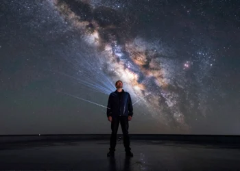 Cada segundo, cien billones de partículas del cosmos atraviesan tu cuerpo sin que lo notes 2 Hombre de mediana edad bajo un cielo estrellado con partículas cósmicas atravesando su cuerpo como hilos de luz azul